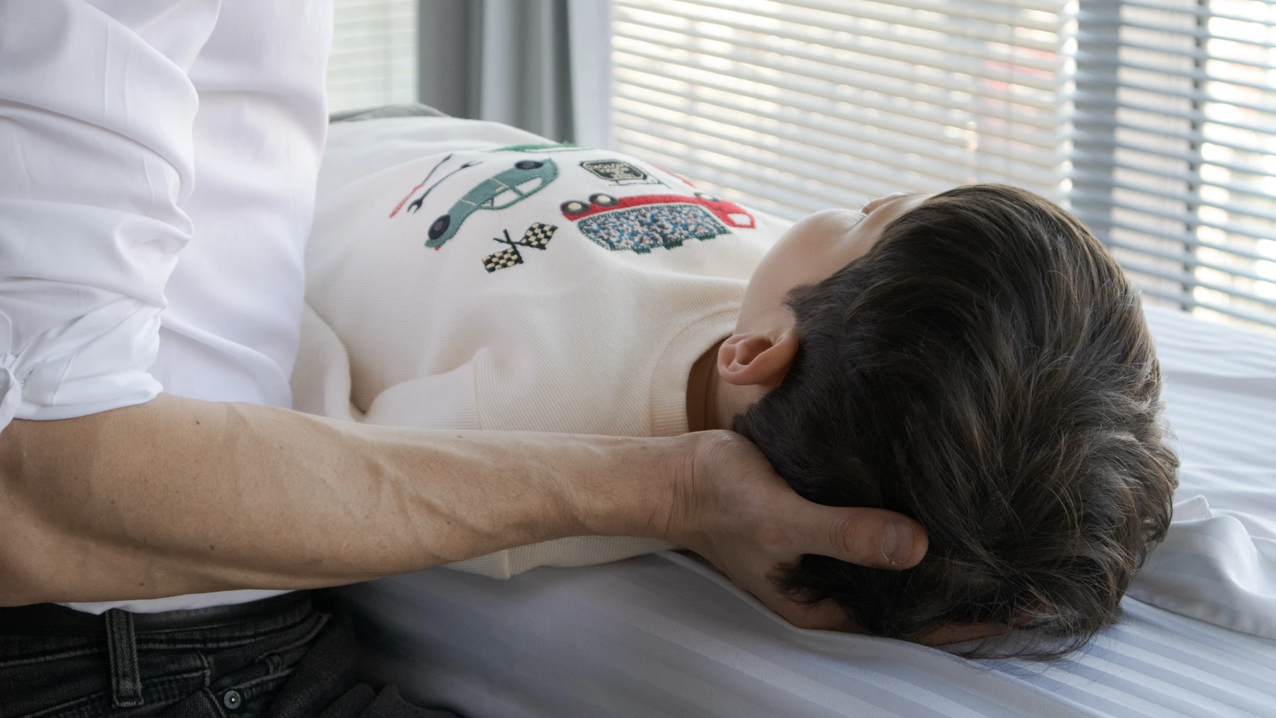 Close view of David Brisson's forearm and open hand supporting the back of a young child&rsquo;s head as the child rests on the treatment table.