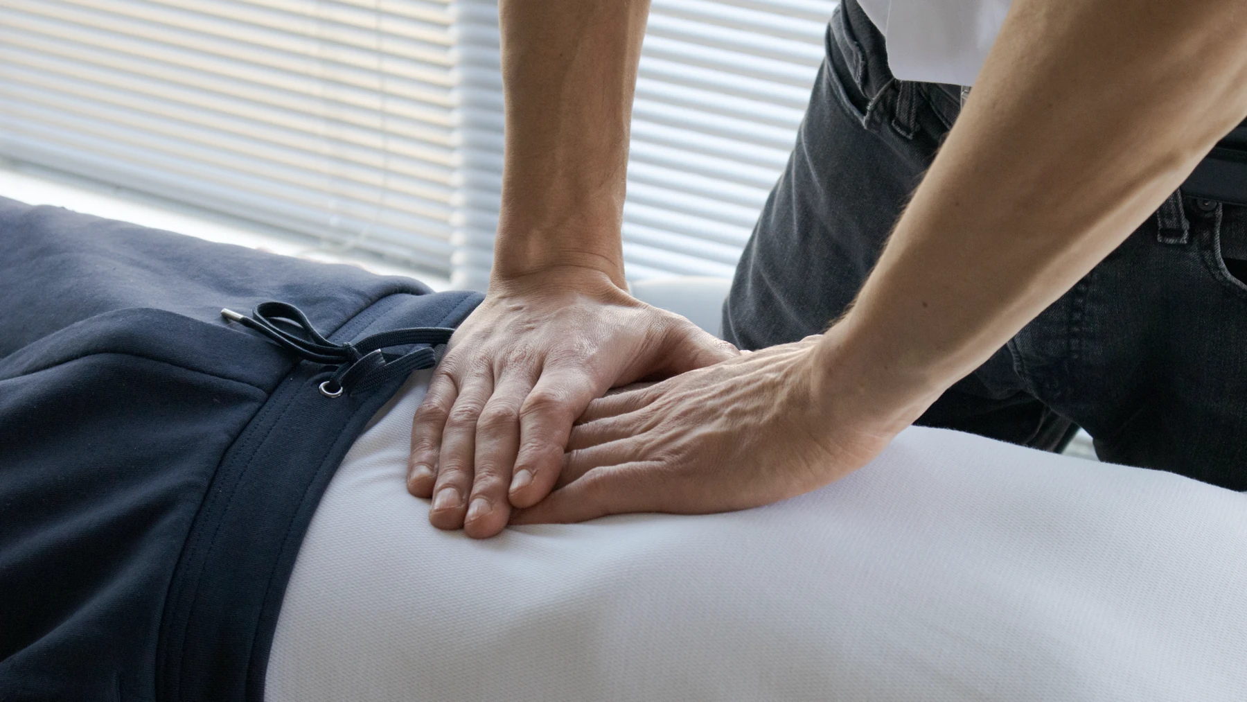 Close view of David Brisson's hands resting flat and still over the sacrum of a patient lying face down on the treatment table.